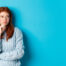How overthinking ruins relationships: Thoughtful and upset redhead girl looking right, pondering solution, standing in sweater against blue background